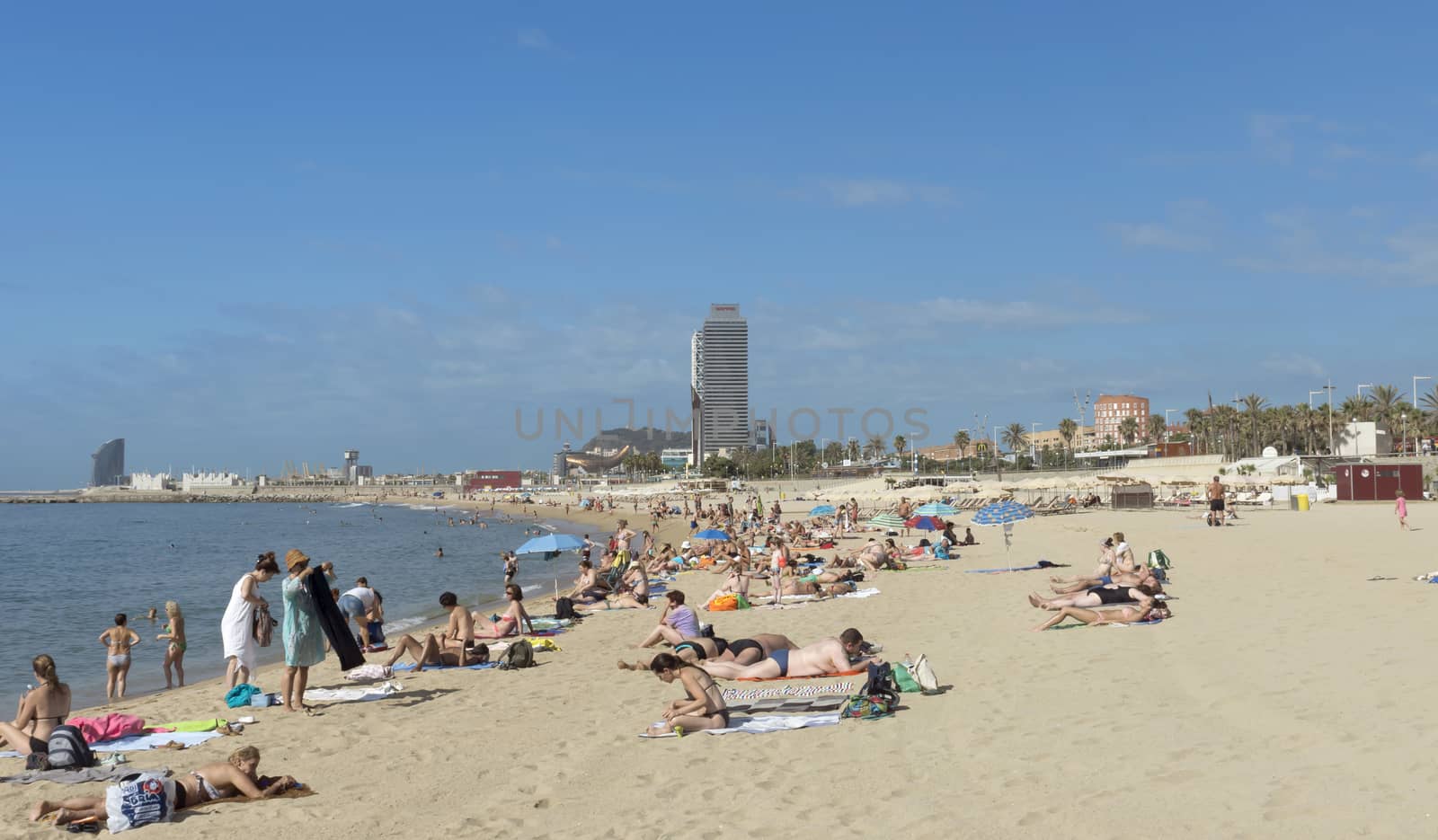 BARCELONA, SPAIN - JULY 9, 2015: Barceloneta Beach and skyscraper Torre Mapfre in the Olympic Port. It is named after its owner, Mapfre, an insurance company. This tower holds the title for highest helipad in Spain at 505 feet above ground.

Barcelona, Spain - July 9, 2015: Barceloneta Beach and skyscraper Torre Mapfre in the Olympic Port. It is named after its owner, Mapfre, an insurance company. This tower holds the title for highest helipad in Spain at 505 feet above ground. People are resting on the beach.