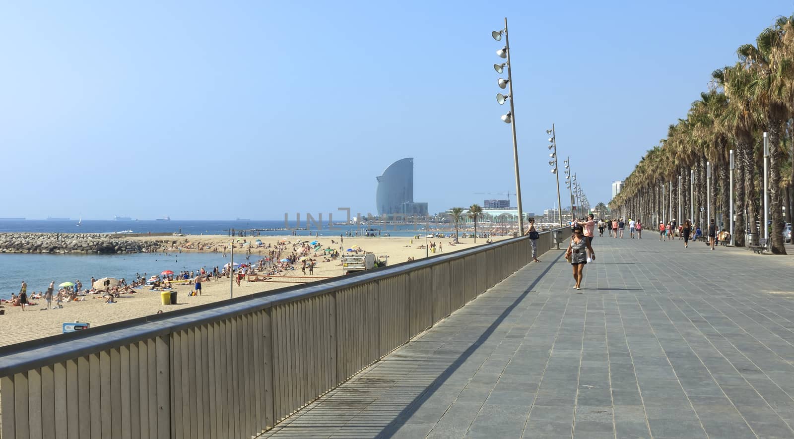 BARCELONA, SPAIN - JULY 12, 2015: View of Barceloneta Beach from Promenade. Barceloneta Beach - one of the most popular in the city.

Barcelona, Spain - July 12, 2015: View of Barceloneta Beach from Promenade. Barceloneta Beach - one of the most popular in the city. People are walking by Barceloneta Palm road.