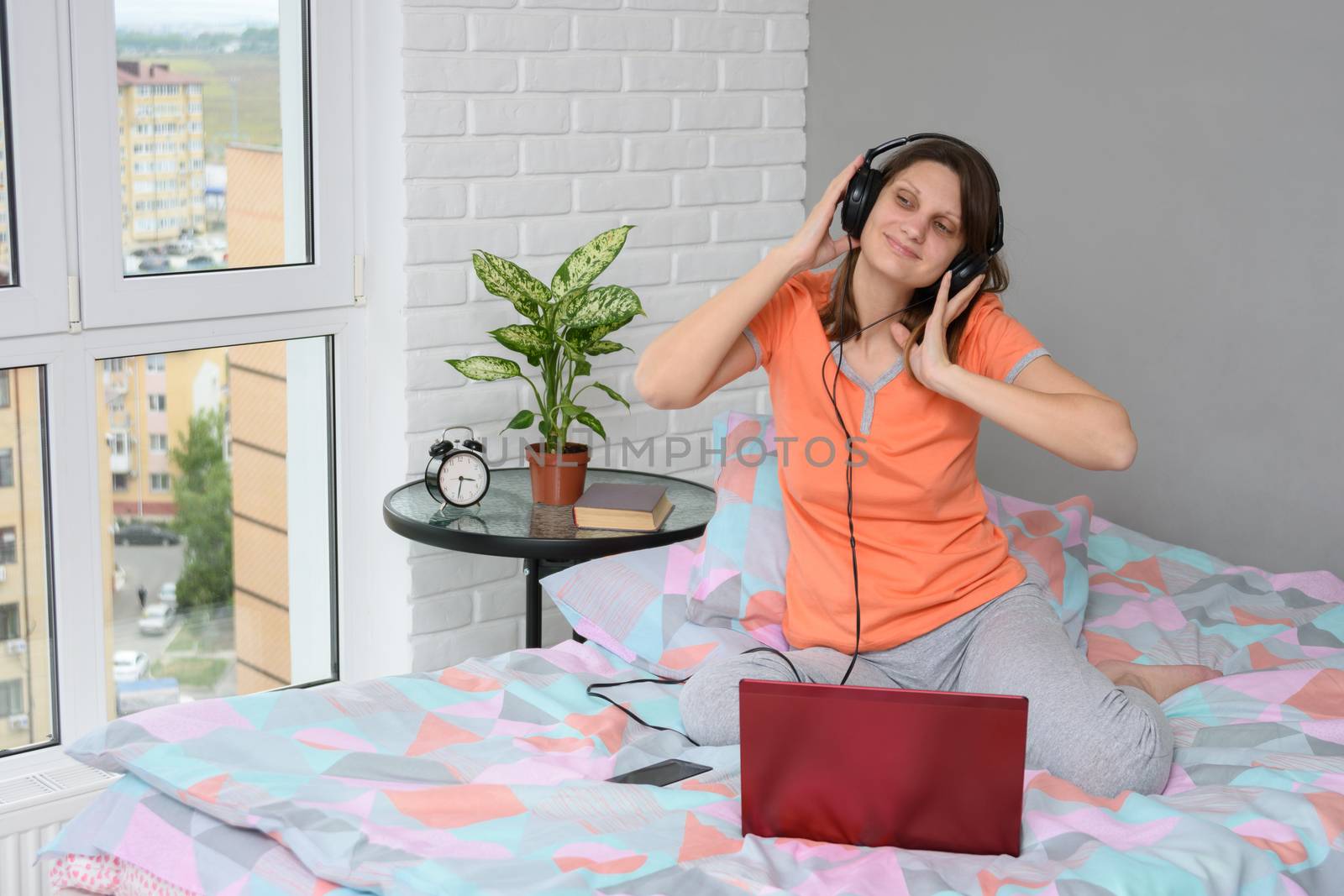 Girl listening to a lecture in headphones sitting at home on the bed by Madhourse