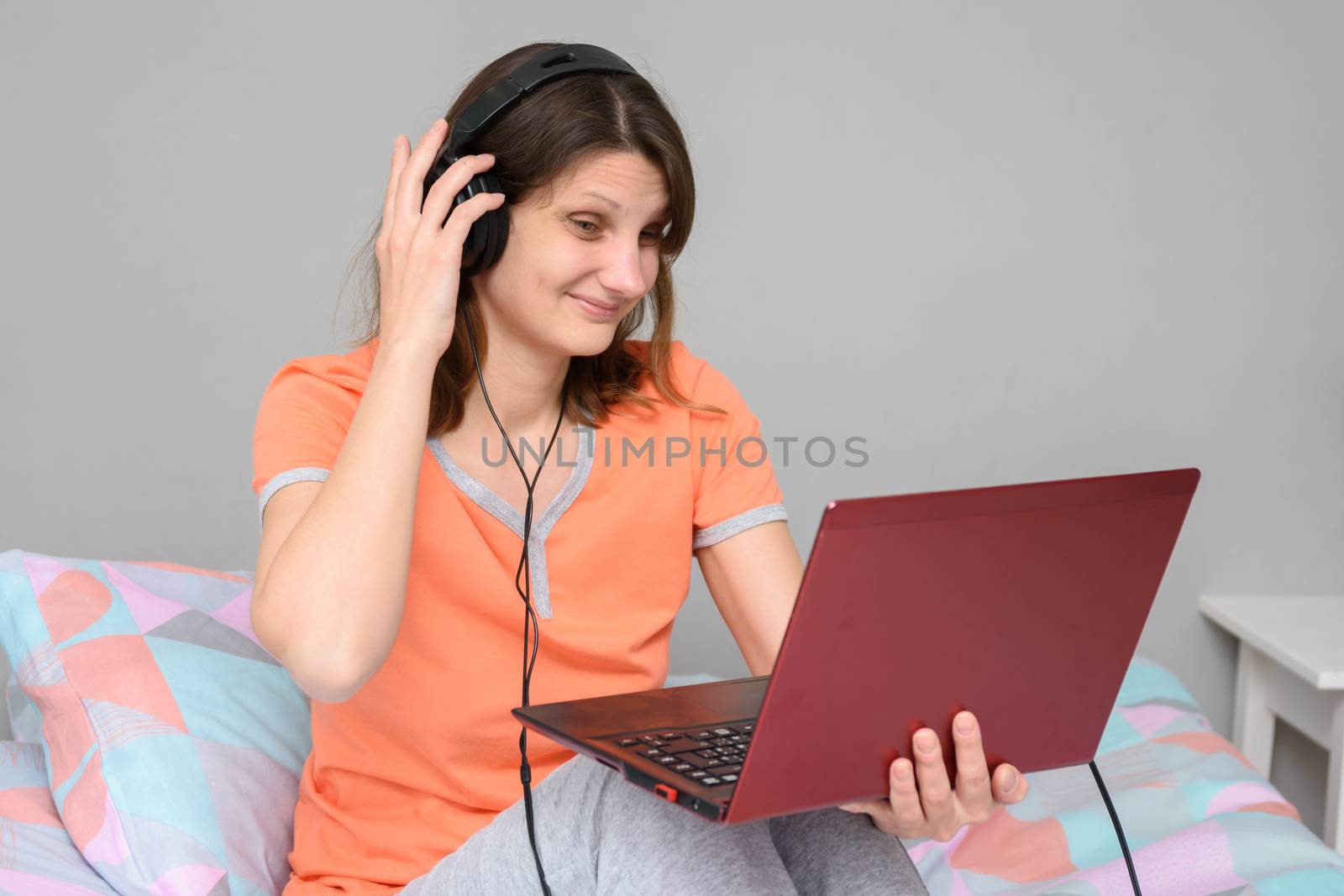 Girl straightens headphones while sitting on bed with laptop