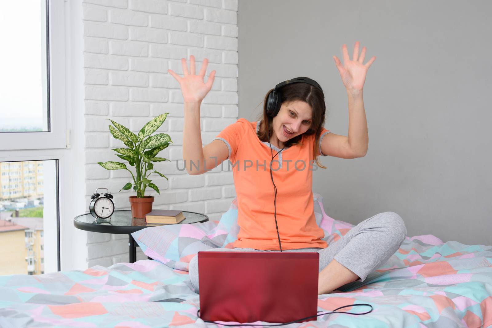 The girl is funny and welcoming waving her hands while looking at the laptop screen