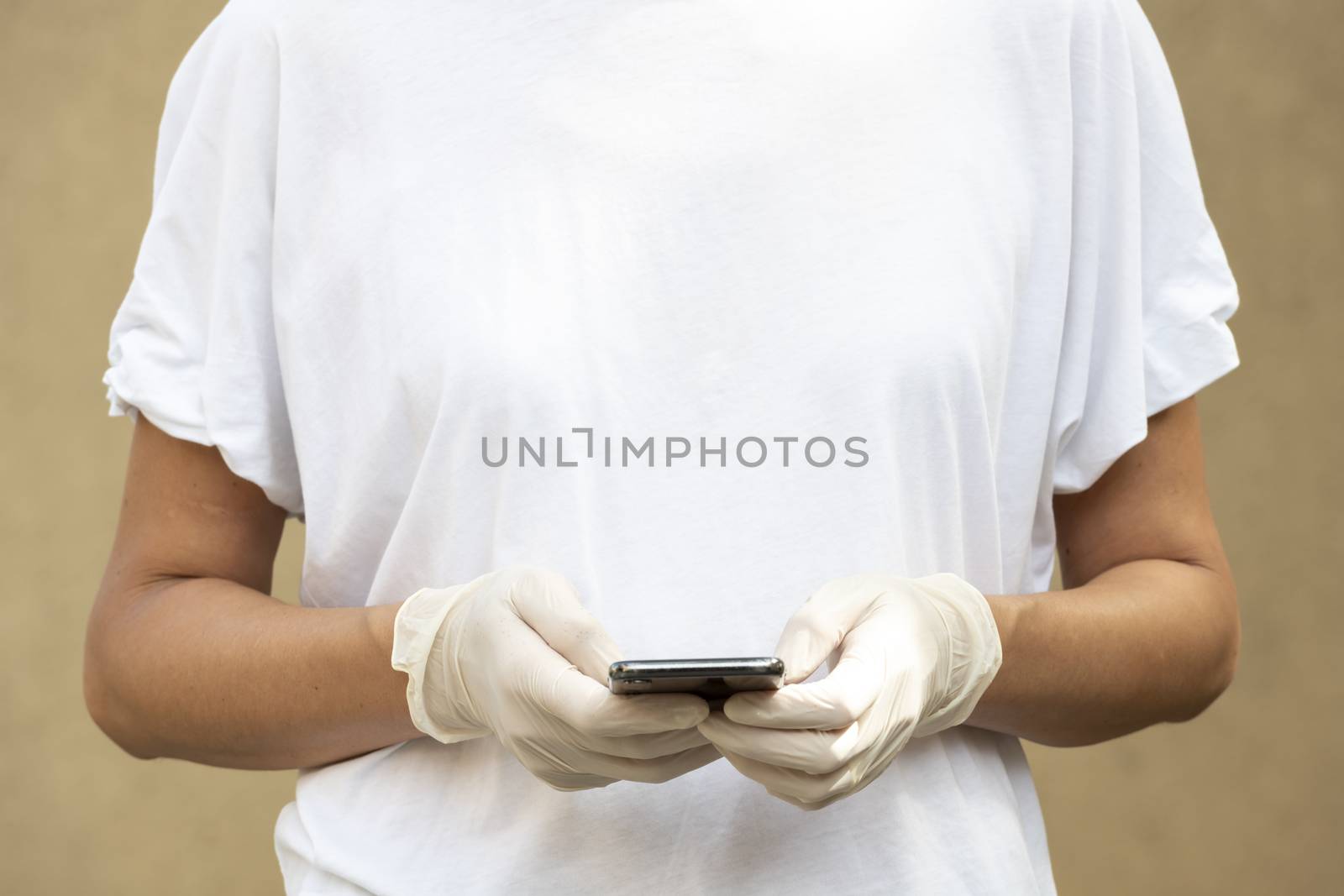 Woman wearing protective gloves and texting or chatting with her Smartphone. Close-up on hands, natural lighting and copy space on womans' t-shirt