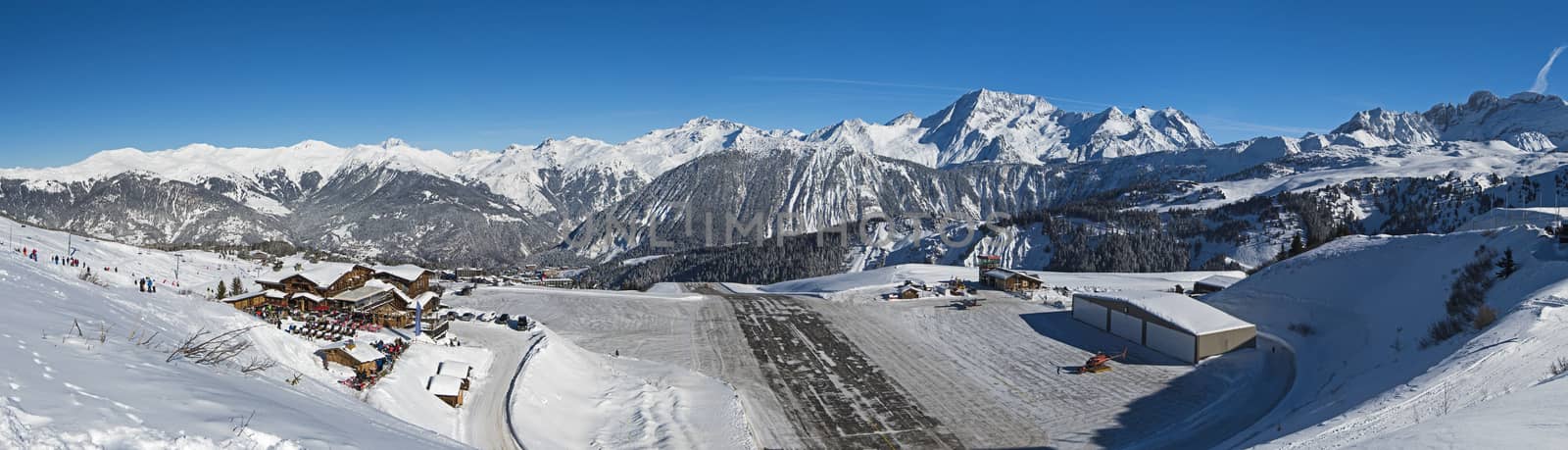 Panoramic landscpae view of small airport altiport runway on the side of a snow covered alpine mountain range in winter