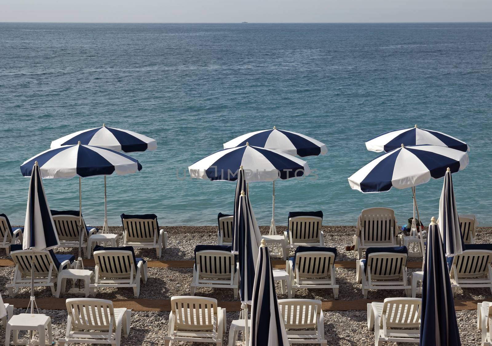 Beach with white and blue umbrellas near Promenade des Anglais in city of Nice, France.