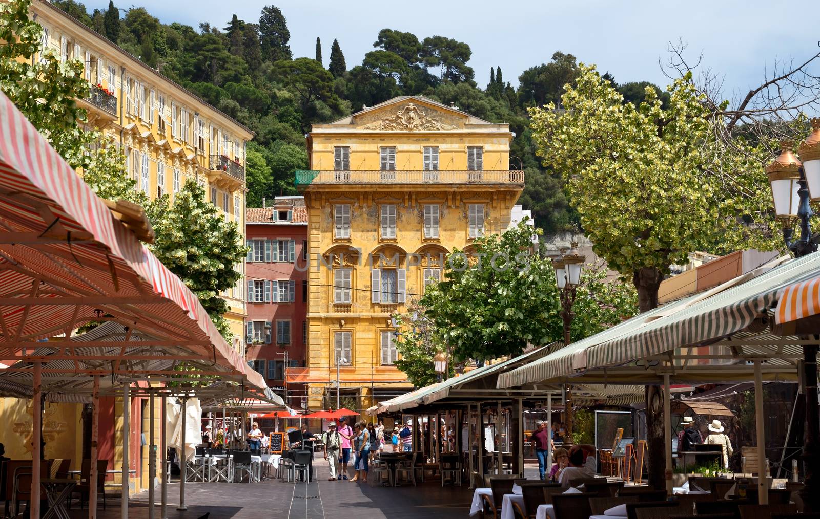 NICE, FRANCE - JUNE 6, 2014: Old building and a cafe in the Cours Saleya. The Cours Saleya is a place of outdoor restaurants, boutiques and a market.

Nice, France - June 6, 2014: Old building and a cafe in the Cours Saleya. The Cours Saleya is a place of outdoor restaurants, boutiques and a market. People are walking by street.