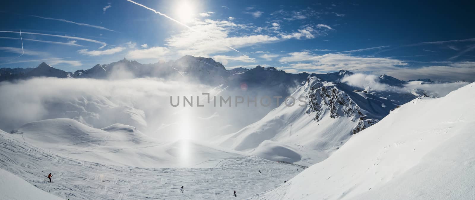 Panoramic view down snow covered valley in alpine mountain range with frost and sunlight sundog in air over ski piste