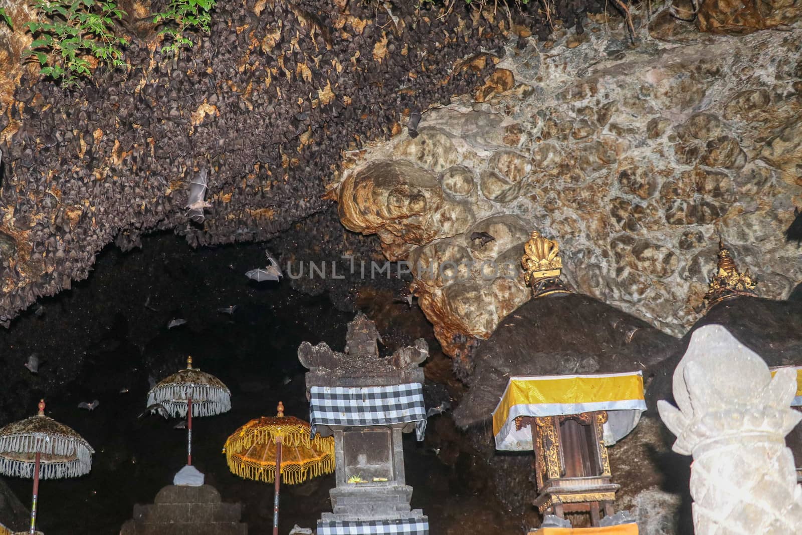 Altars at Pura Goa Lawah or Bat Cave Temple. Balinese Hindu temple, Klungkung, Bali, Indonesia. Some bats fly under a rock overhang. Colony of bats hanging from the ceiling and are waiting dark.