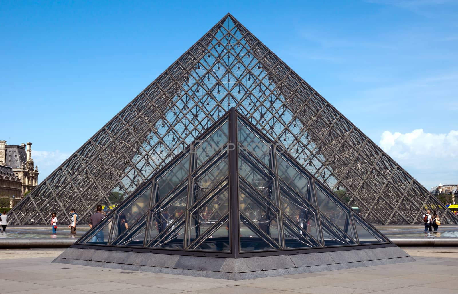 PARIS, FRANCE - JUNE 9: Pyramid near Louvre Museum on June 9, 2014 in Paris, France. Louvre is one of the biggest Museum in the world, receiving more than 8 million visitors each year. 

Paris, France - June 9, 2014: Pyramid near Louvre Museum. Louvre is one of the biggest Museum in the world, receiving more than 8 million visitors each year. People are walking near pyramid.