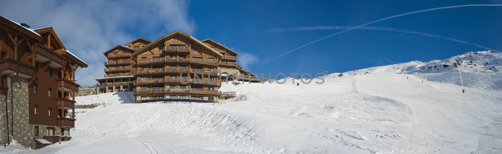 Panoramic view of snow covered piste in an alpine ski resort with apartment buildings on slope