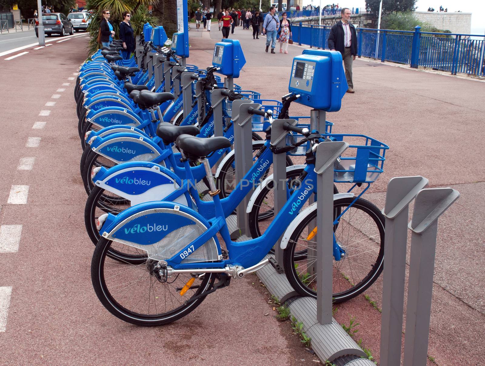 NICE, FRANCE - APRIL 27: Public Bicycles Sharing Station on April 27, 2013 in Nice, France. One of 120 stations in Nice. This service offers over 1200 self-service bicycles.

Nice, France - April 27, 2013: Row of public bikes for rent along the street. People are walking. Nice has 120 stations. This service offers over 1200 self-service bicycles.