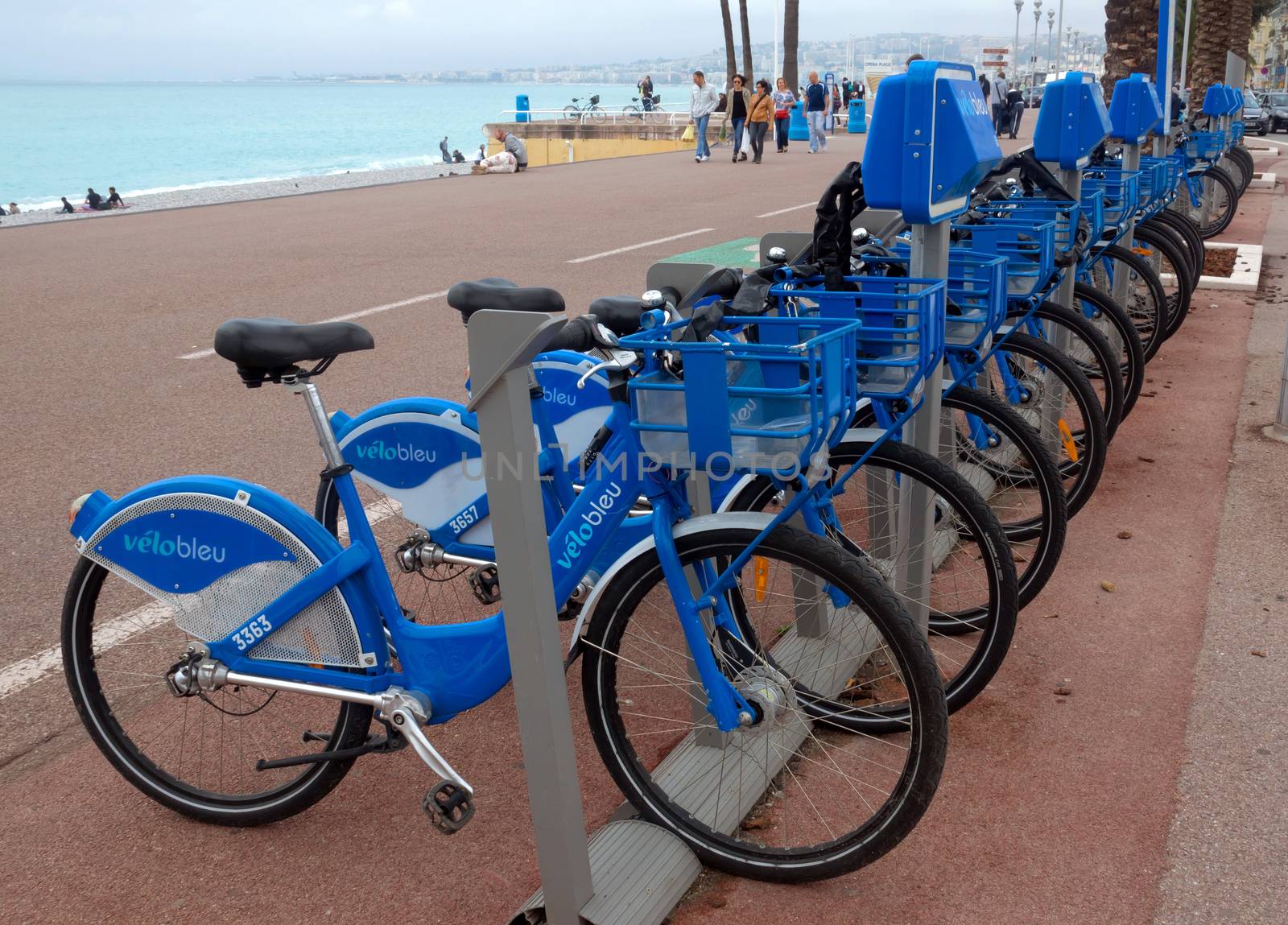 NICE, FRANCE - APRIL 27: Public Bicycles Sharing Station on April 27, 2013 in Nice, France. One of 120 stations in Nice. This service offers over 1200 self-service bicycles.

Nice, France - April 27, 2013: Row of public bikes for rent along the street. People are walking. Nice has 120 stations. This service offers over 1200 self-service bicycles. People are walking by Promenade.