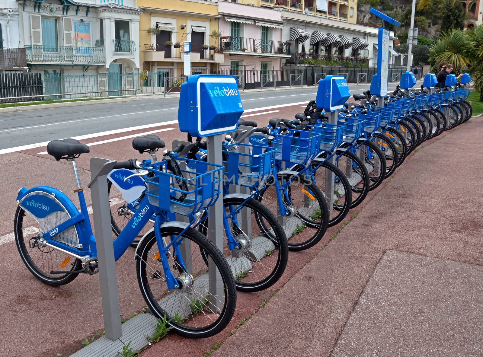 NICE, FRANCE - APRIL 27: Public Bicycles Sharing Station on April 27, 2013 in Nice, France. One of 120 stations in Nice. This service offers over 1200 self-service bicycles.

Nice, France - April 27, 2013: Row of public bikes for rent along the street. People are walking. Nice has 120 stations. This service offers over 1200 self-service bicycles. People take a bicycle.
