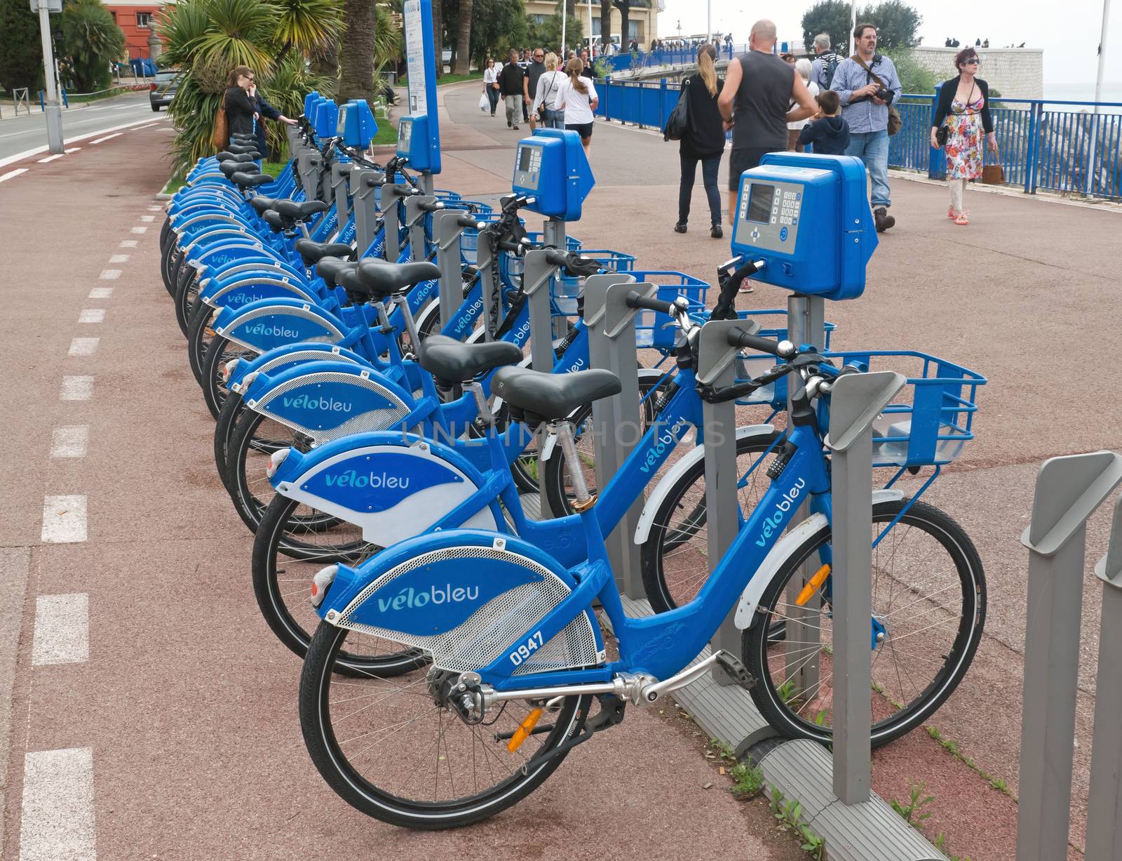 NICE, FRANCE - APRIL 27: Public Bicycles Sharing Station on April 27, 2013 in Nice, France. One of 120 stations in Nice. This service offers over 1200 self-service bicycles.

Nice, France - April 27, 2013: Row of public bikes for rent along the street. People are walking. Nice has 120 stations. This service offers over 1200 self-service bicycles.