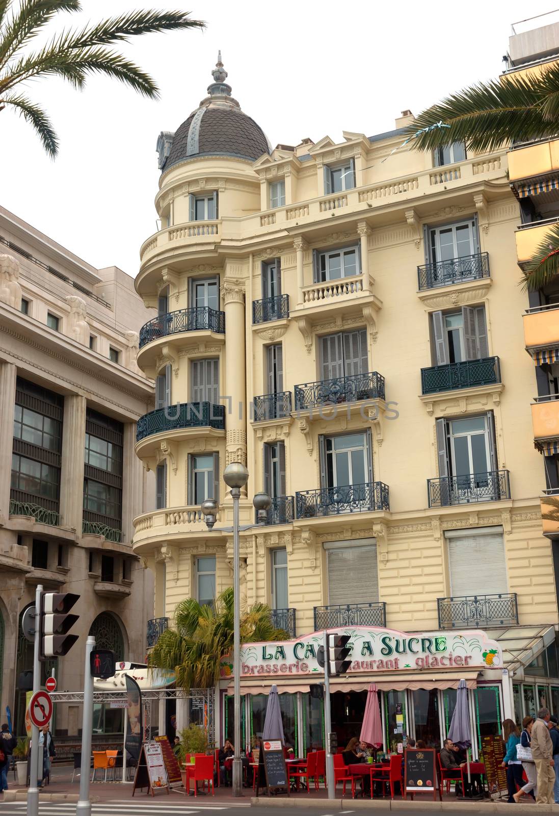 NICE, FRANCE - APRIL 27: Architecture along Promenade des Anglais on April 27, 2013 in Nice, France. It is a symbol of the Cote d'Azur and was built in 1830 at the expense of the British colony.

Nice, France - April 27, 2013: Architecture along Promenade des Anglais. Promenade des Anglais is a symbol of the Cote d'Azur and was built in 1830 at the expense of the British colony. People are resting in cafe.