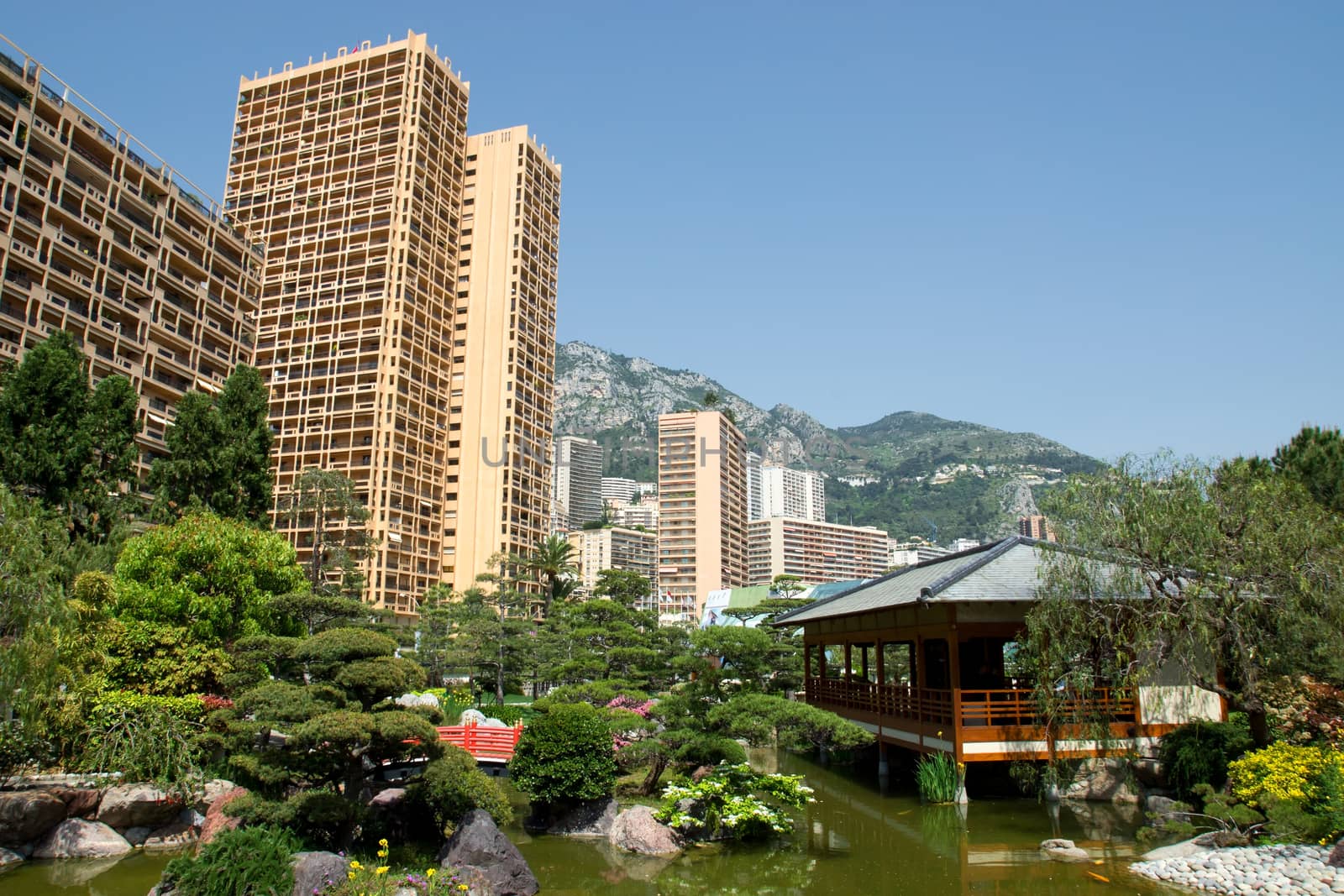 Japanese garden of Monaco, with a japanese house and a pond and Monte Carlo buildings behind. 