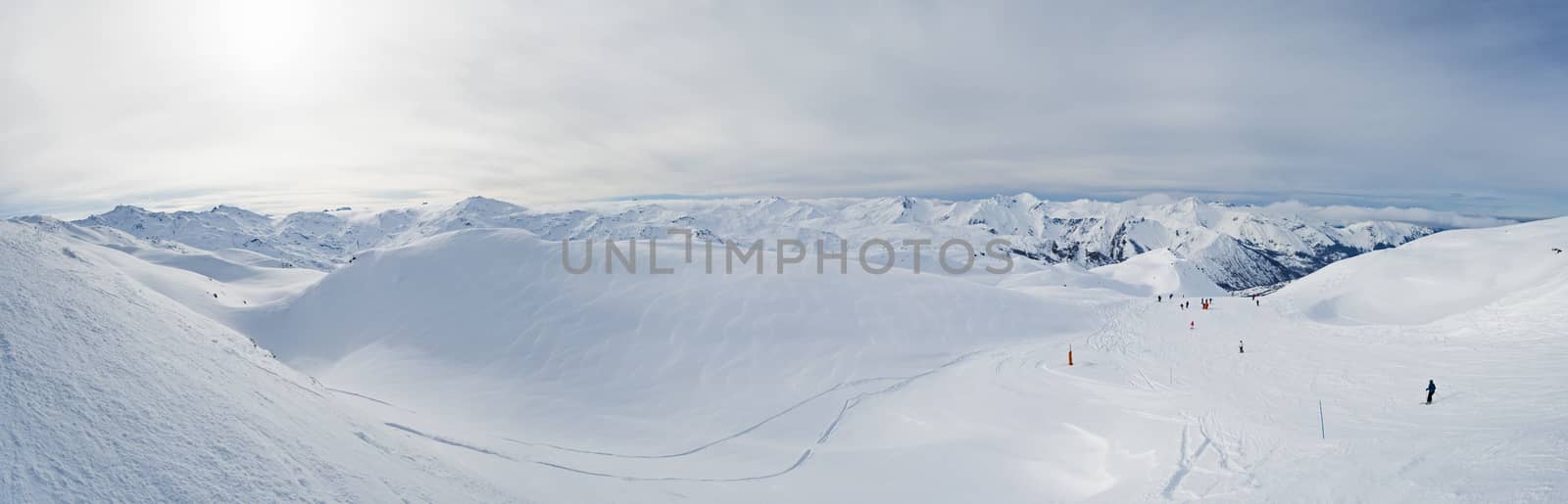 Panoramic view across snow covered alpine mountain range in alps with ski piste