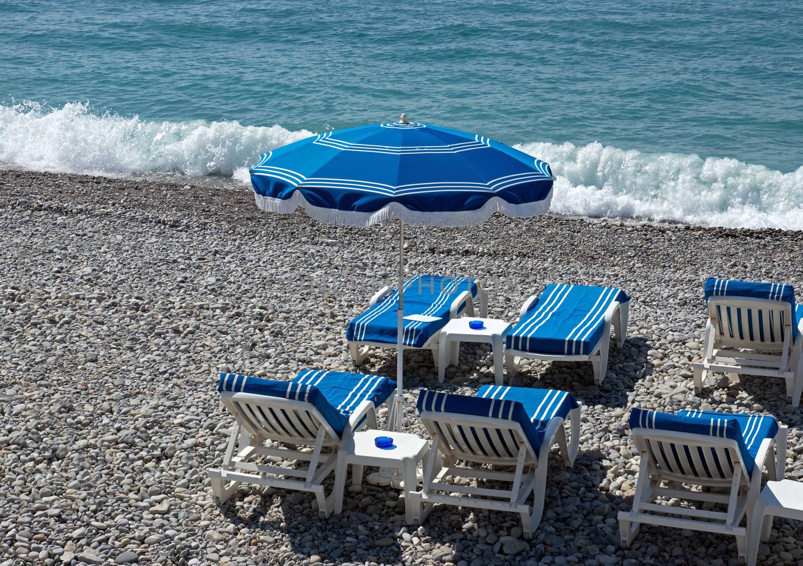 Beach with blue umbrella near Promenade des Anglais in city of Nice, France.