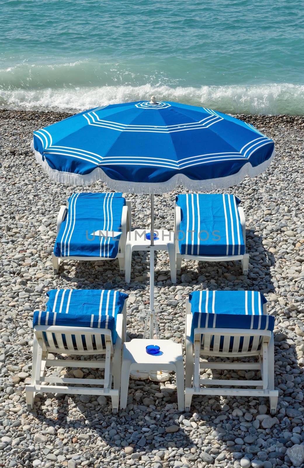 Beach with blue umbrellas near Promenade des Anglais in city of Nice, France.