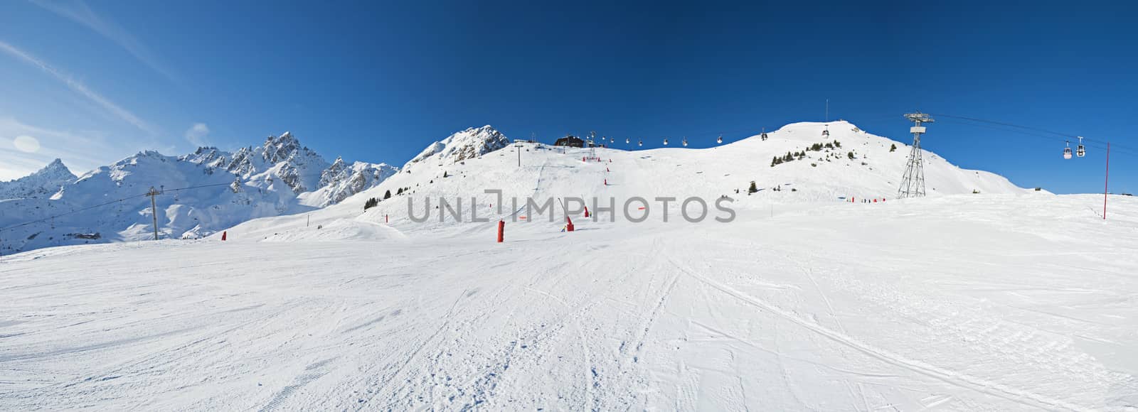 Panoramic landscape up a large ski slope piste in winter alpine mountain resort