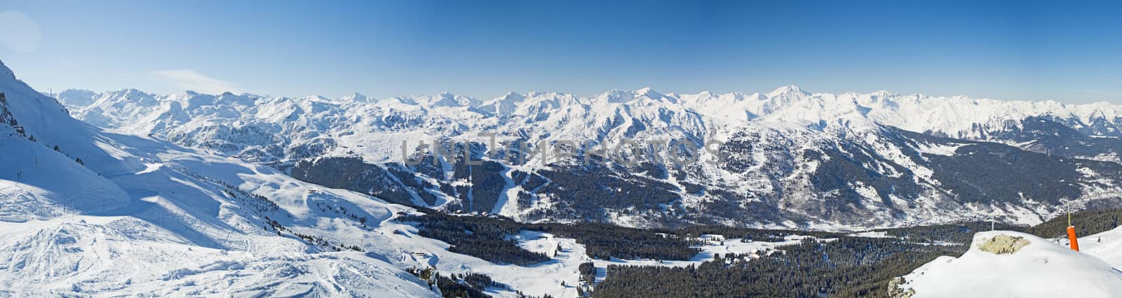Panoramic view across snow covered alpine mountain range in alps on blue sky background