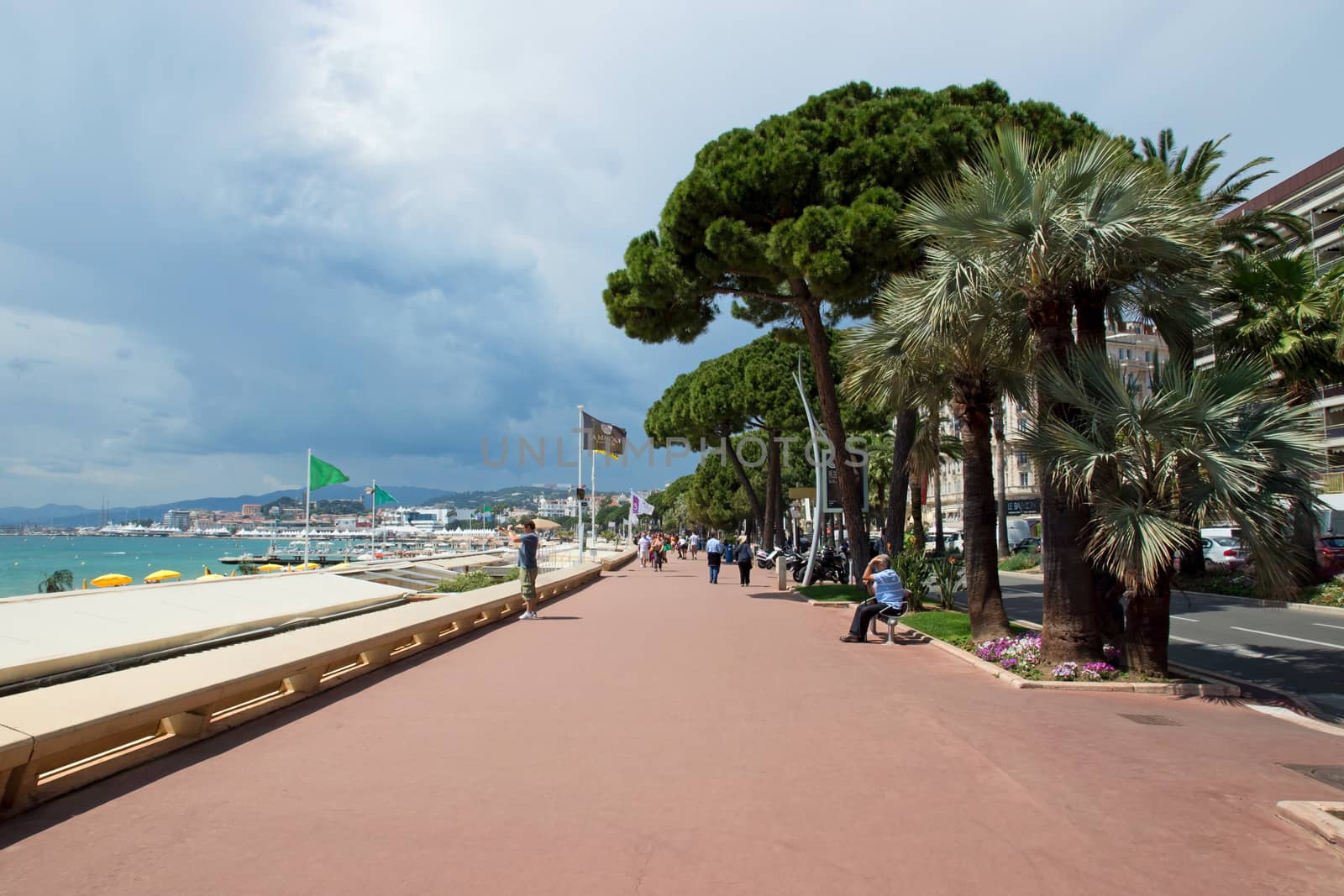 CANNES, FRANCE - MAY 6: Pedestrians walking on the famous "La Croisette" Boulevard on May 6, 2013 in Cannes, France. It is a symbol of the Cote d'Azur.

Cannes, France - May 6, 2013: Pedestrians walking on the famous "La Croisette" Boulevard. It is a symbol of the Cote d'Azur.