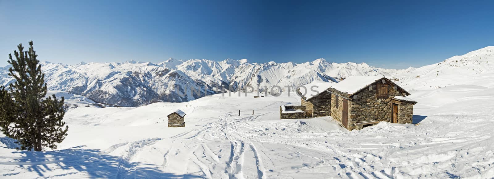 Panoramic view of snow covered mountains in an alpine ski resort with stone building on remote slope