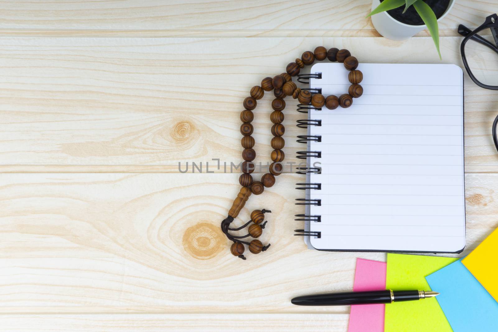 Flat lay view of workspace with Pen, spectacles, decoration flower, rosary and book.Copy Space, business and education concept. 