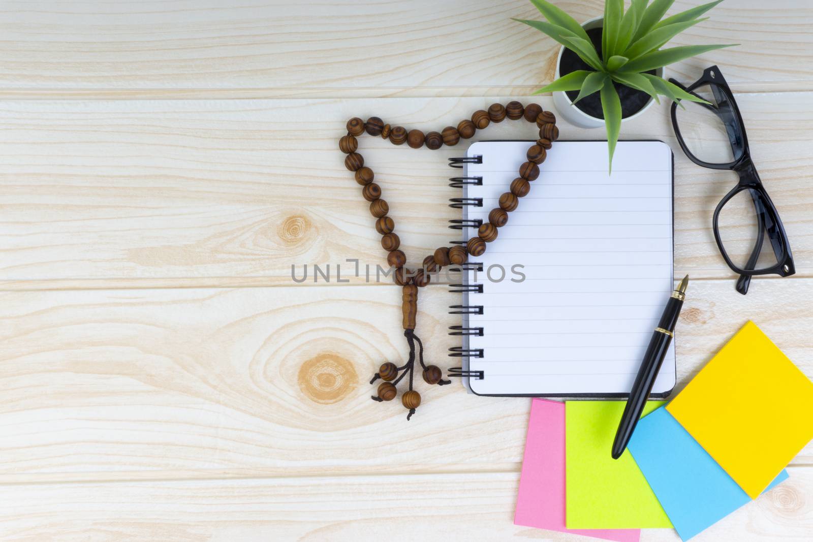 Flat lay view of workspace with Pen, spectacles, decoration flower, rosary and book.Copy Space, business and education concept. 