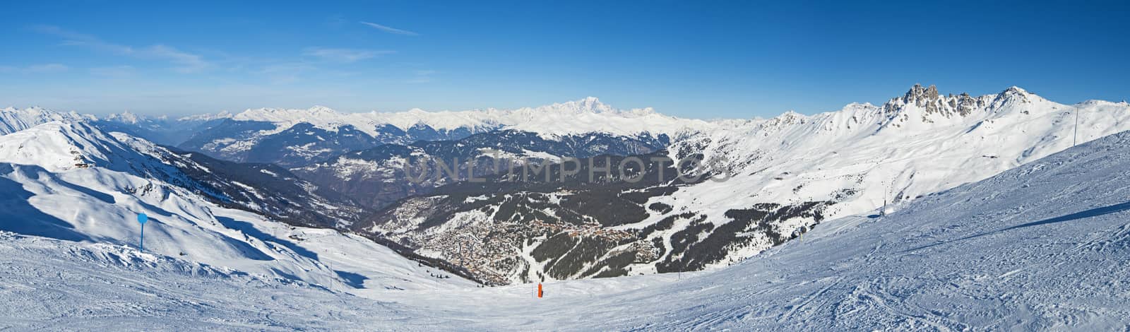 Panoramic view across snow covered alpine mountain range in alps on blue sky background with mountain village