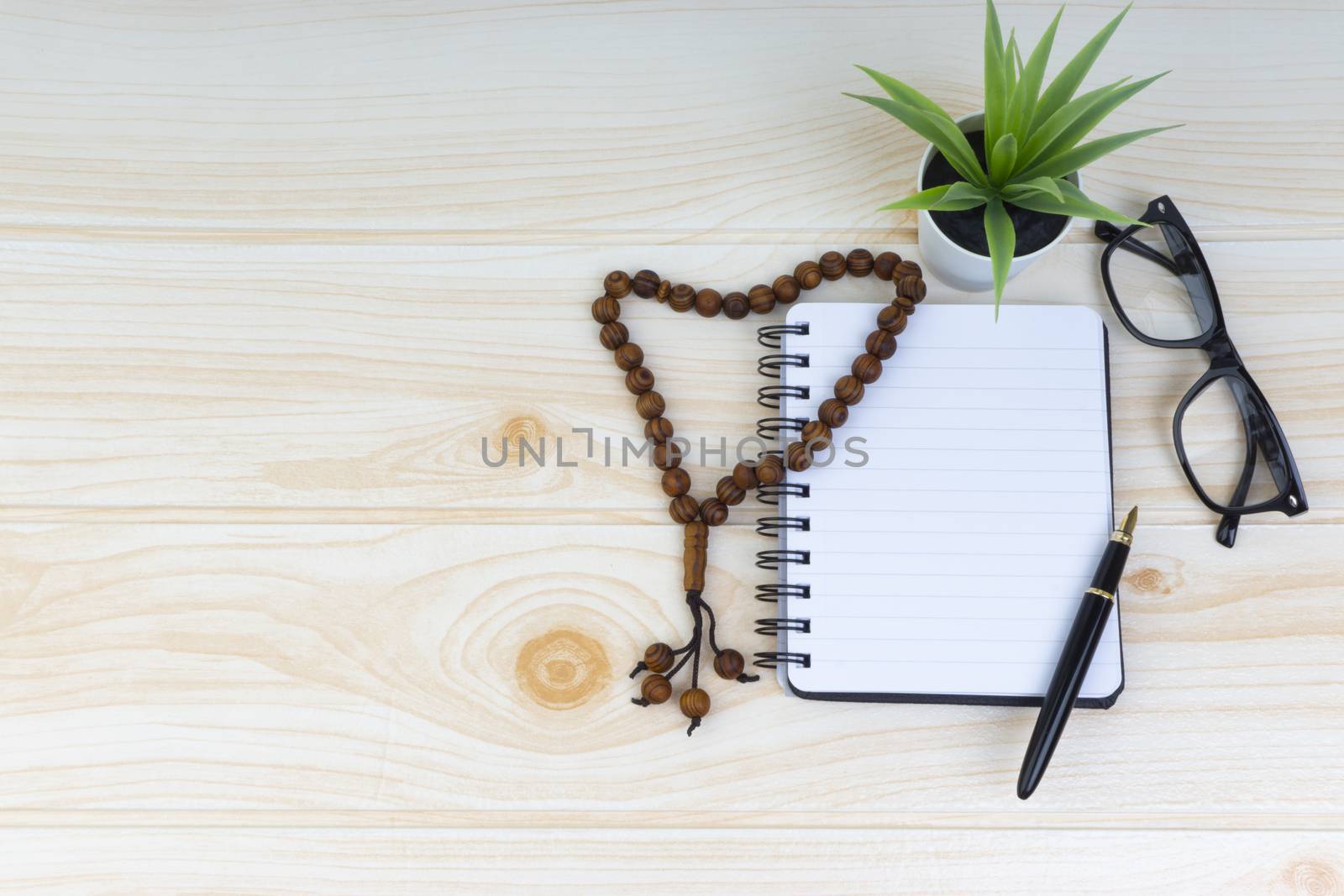 Flat lay view of workspace with Pen, spectacles, decoration flower, rosary and book. Copy Space, business and education concept. 