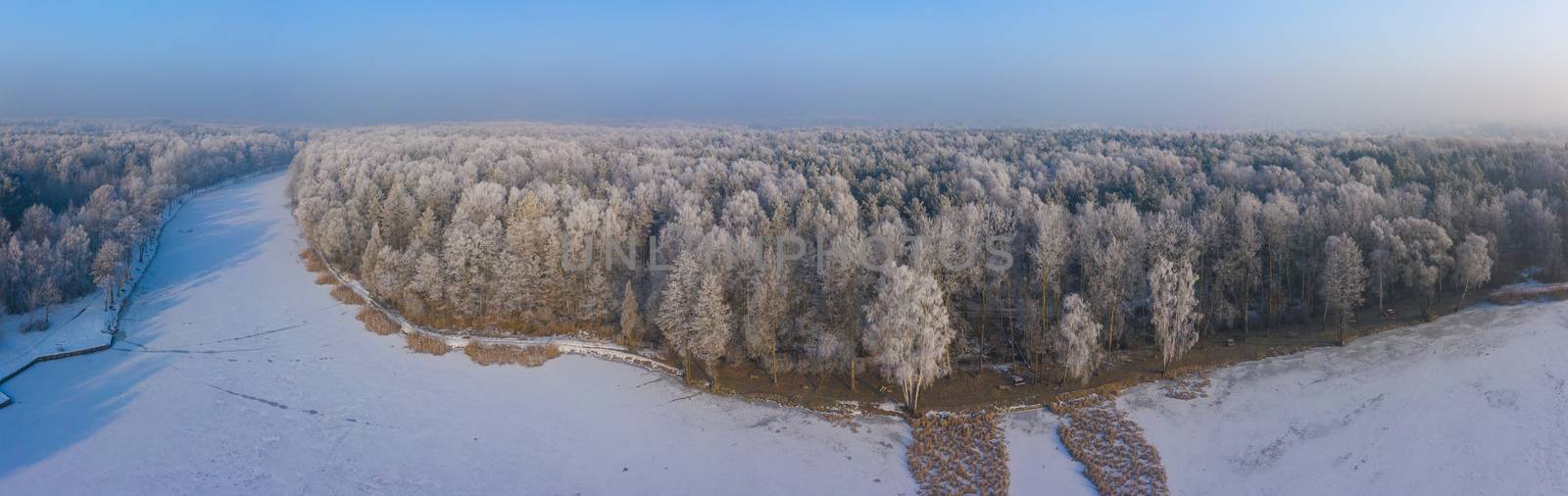 Rime and hoarfrost covering trees. Aerial view of the snow-covered forest and lake from above. Winter scenery. Landscape photo captured with drone.
