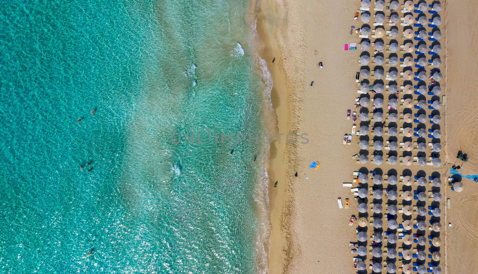 Top down aerial view of amazing beach with umbrellas and turquoise sea at sunset. Mediterranean sea, Crete, Greece.