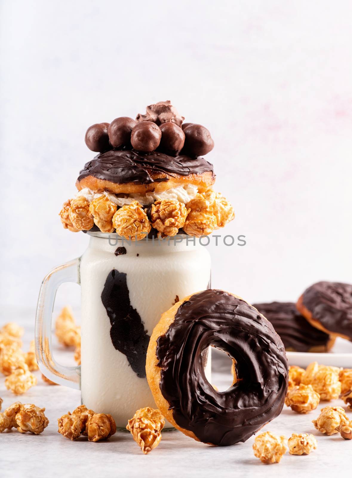 Ice cold chocolate donut milkshake in a mason jar decorated with caramel popcorn, whipped cream and cocoa candies