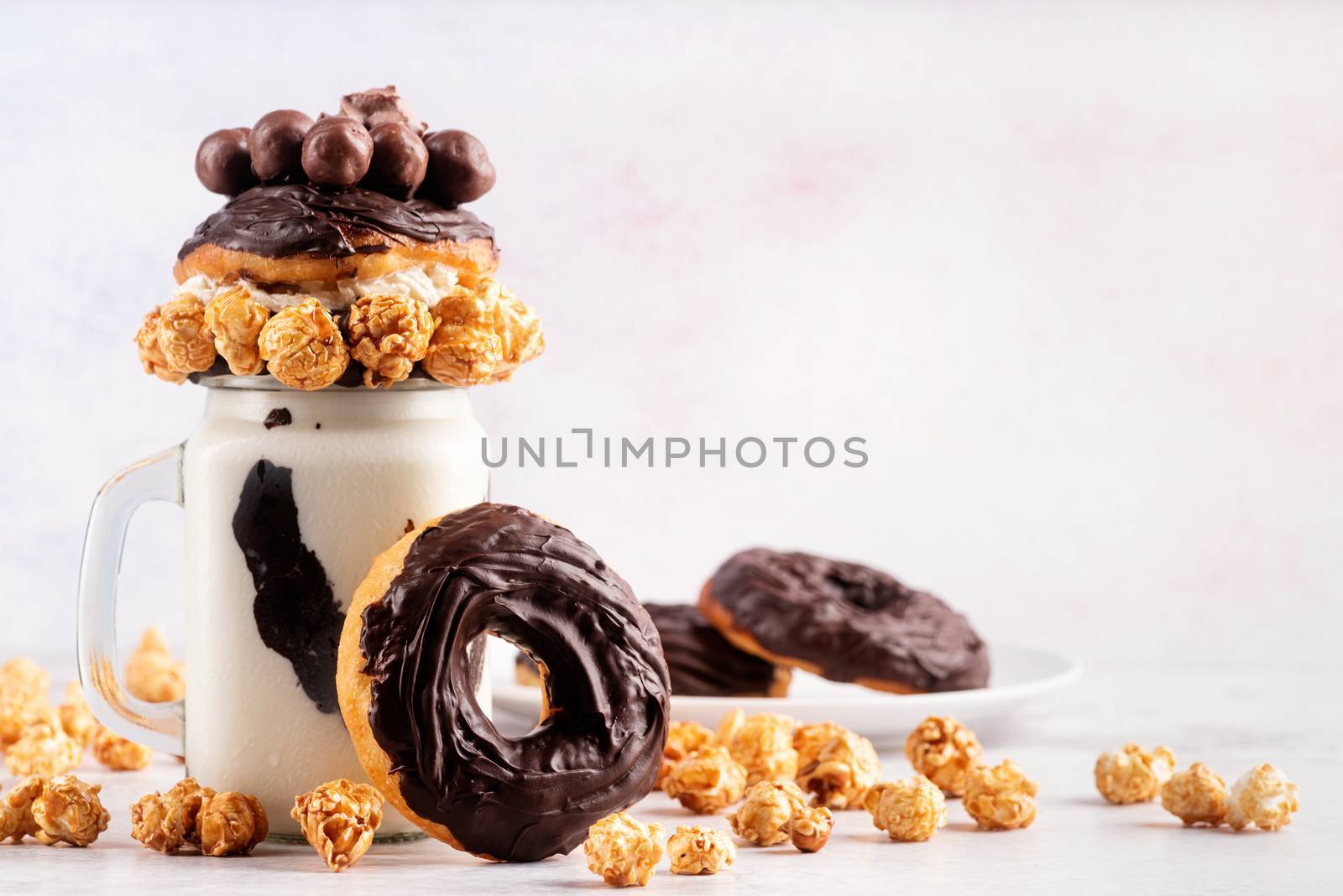 Ice cold chocolate donut milkshake in a mason jar decorated with caramel popcorn, whipped cream and cocoa candies with copy space