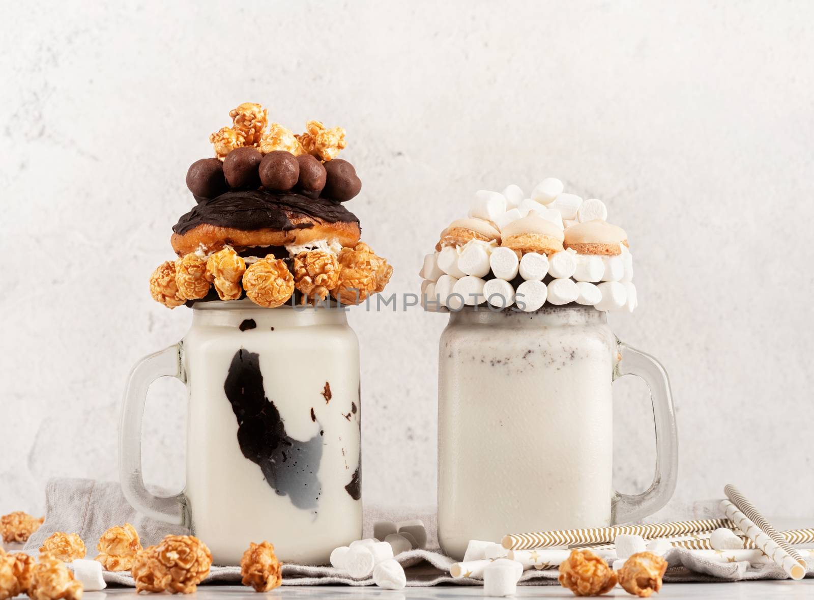 two crazy milkshakes decorated with donuts, popcorn, candies and marshmallows front view by Desperada