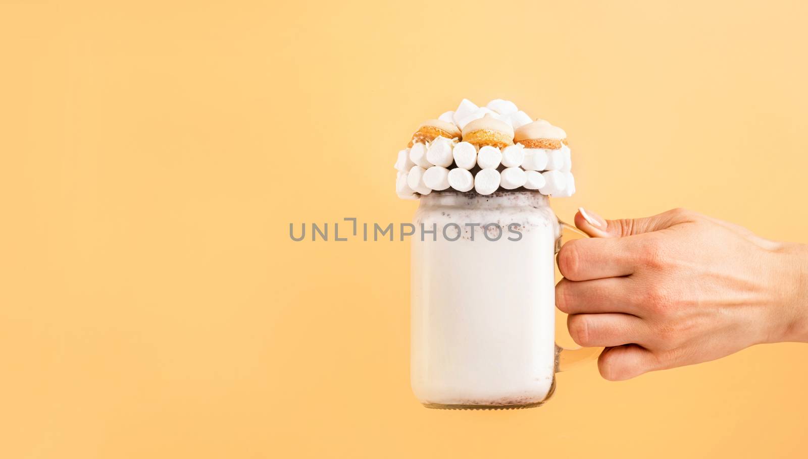 Female hand holding marshmallow freakshake isolated on orange background with copy space