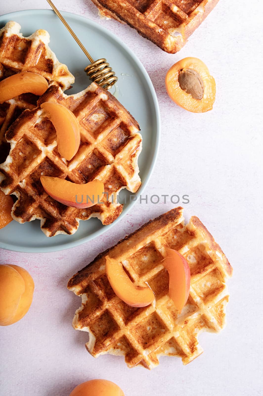 Homemade belgian waffles with apricots and honey on blue plate top view flat lay
