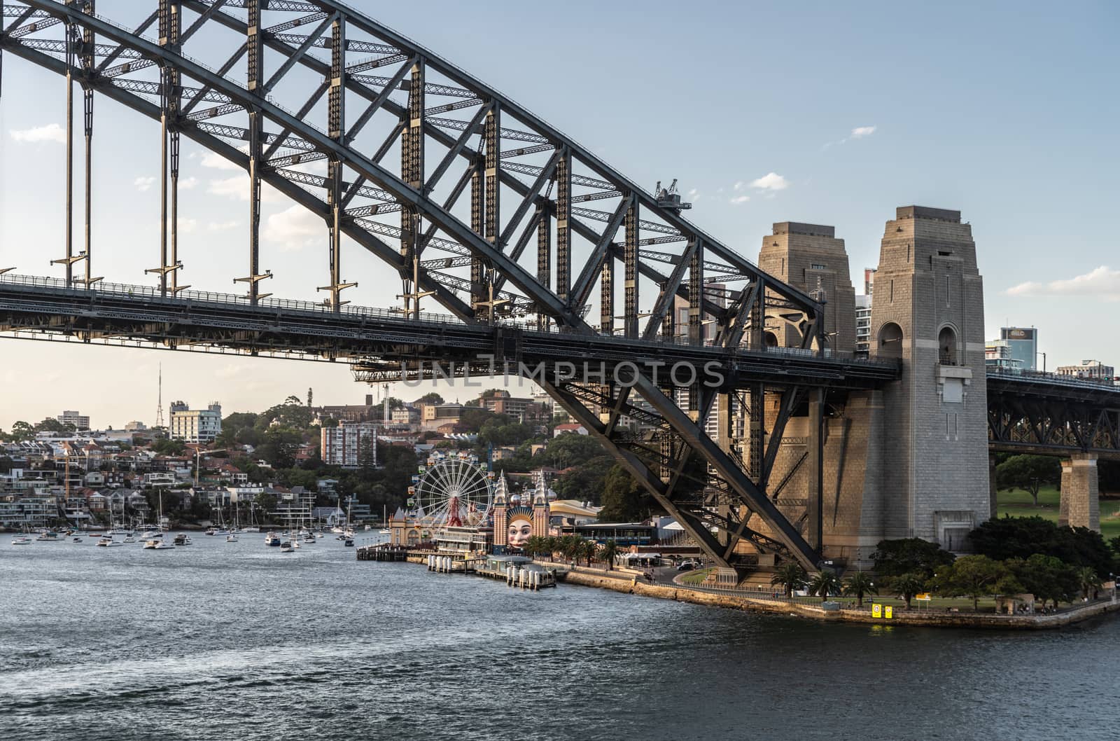 Sydney, Australia - February 12, 2019: Harbour bridge north side landing during sunset. Horizon is north shore of bay with Kirribilli neighborhood and Luna Park. Boats on water.