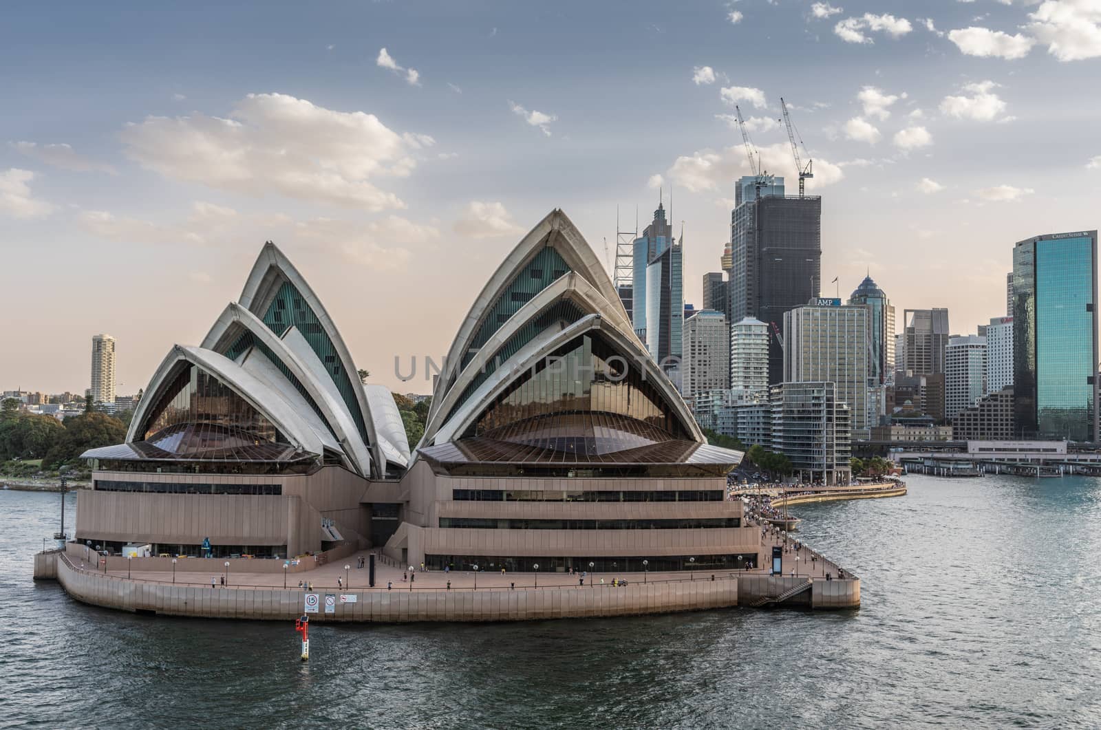 Sydney, Australia - February 12, 2019: North side of the Opera House and city skyline. Light Blue sky and gray water. Circular bay ferry terminal and railway station. Boats in water.