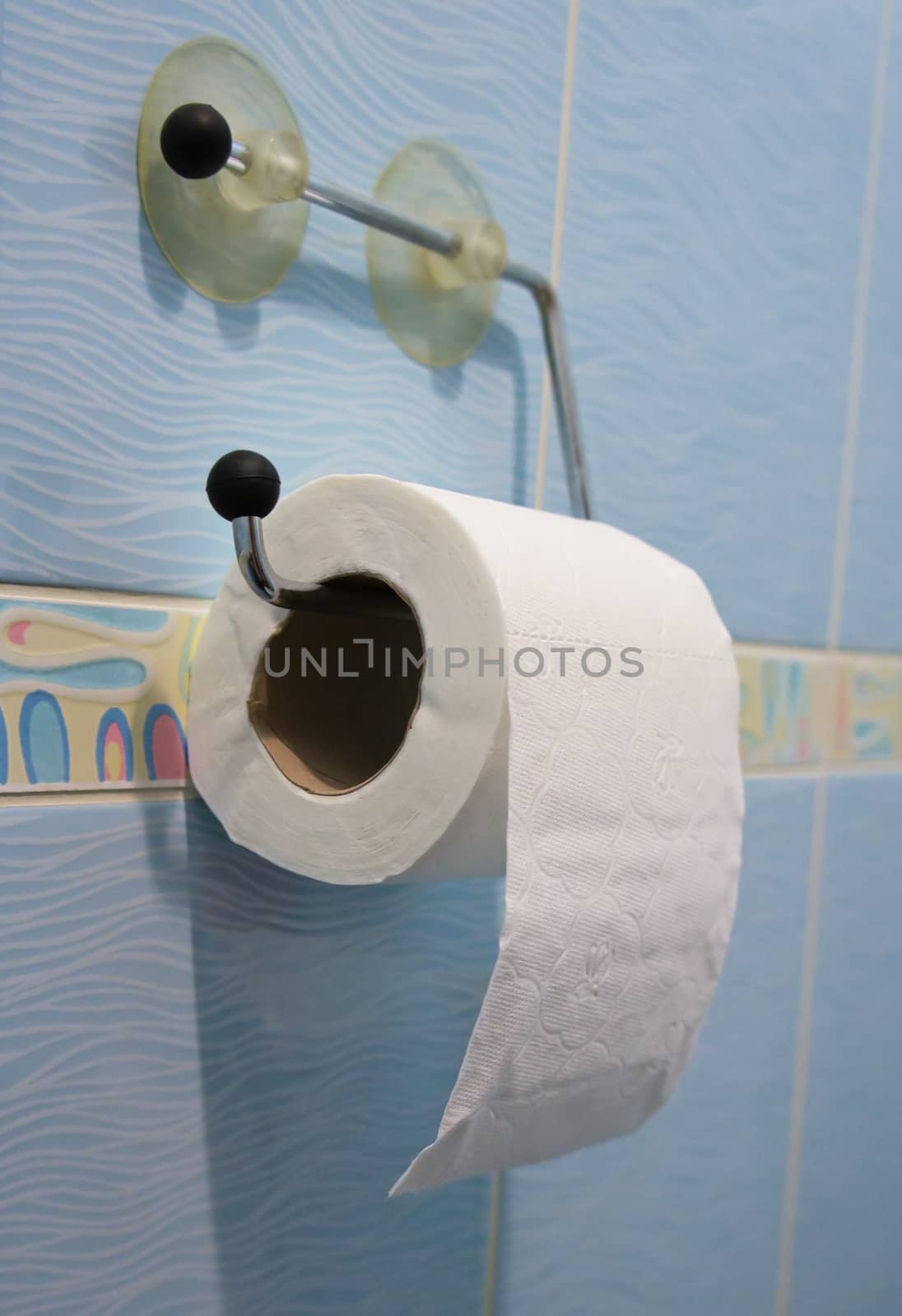 Toilet paper roll hanging over blue ceramic tiles.
