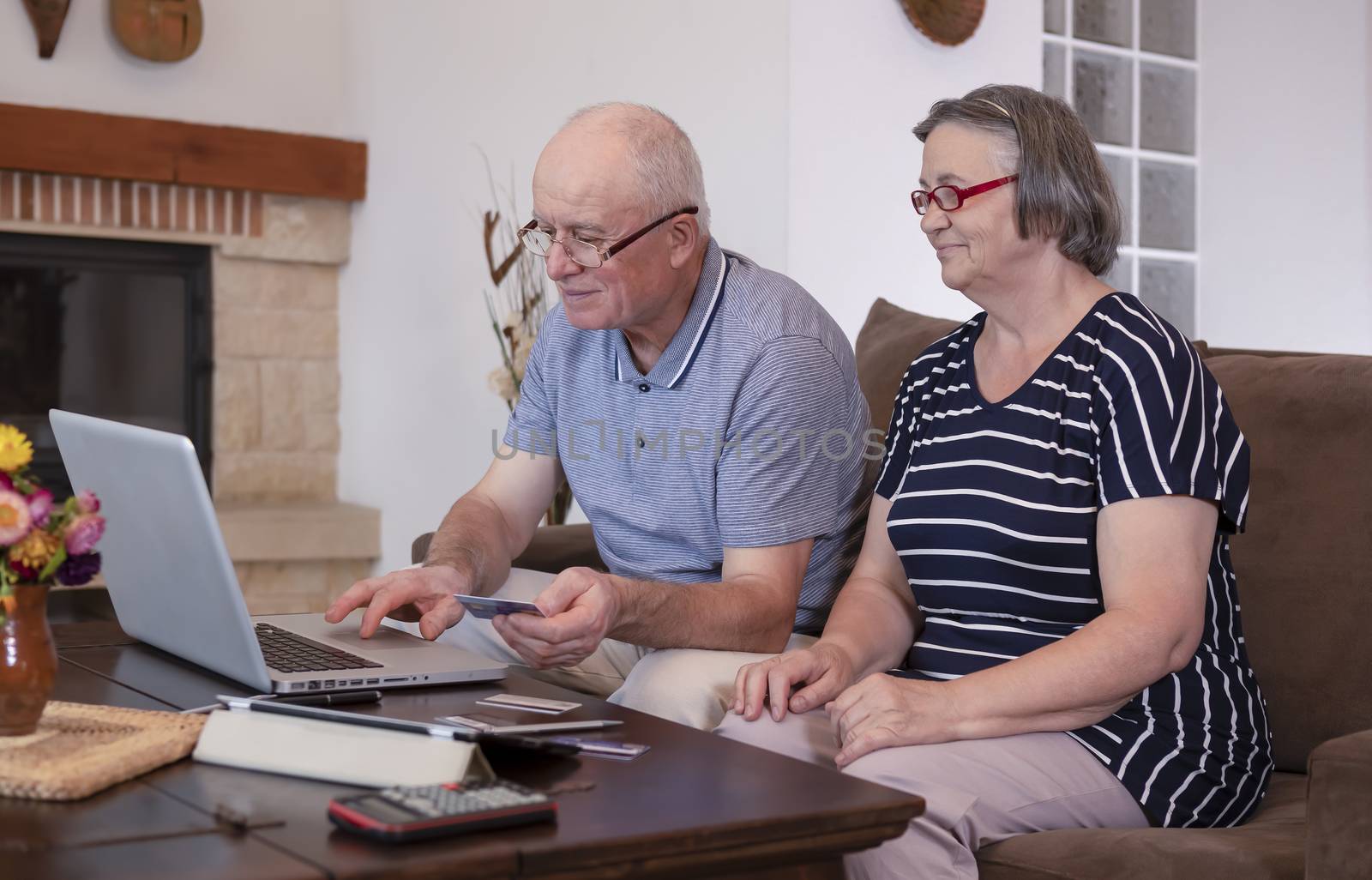 Senior couple shopping online using credit card on laptop by manaemedia