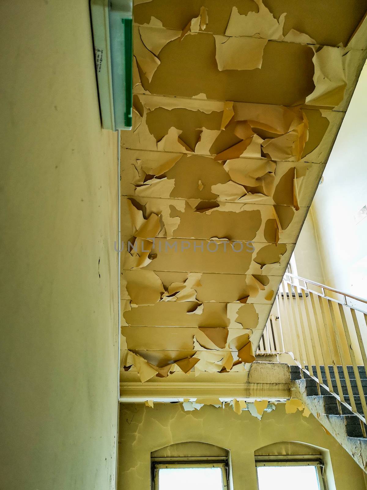 Upward look to peeleng painting of ceiling under stairs in old abandoned hospital