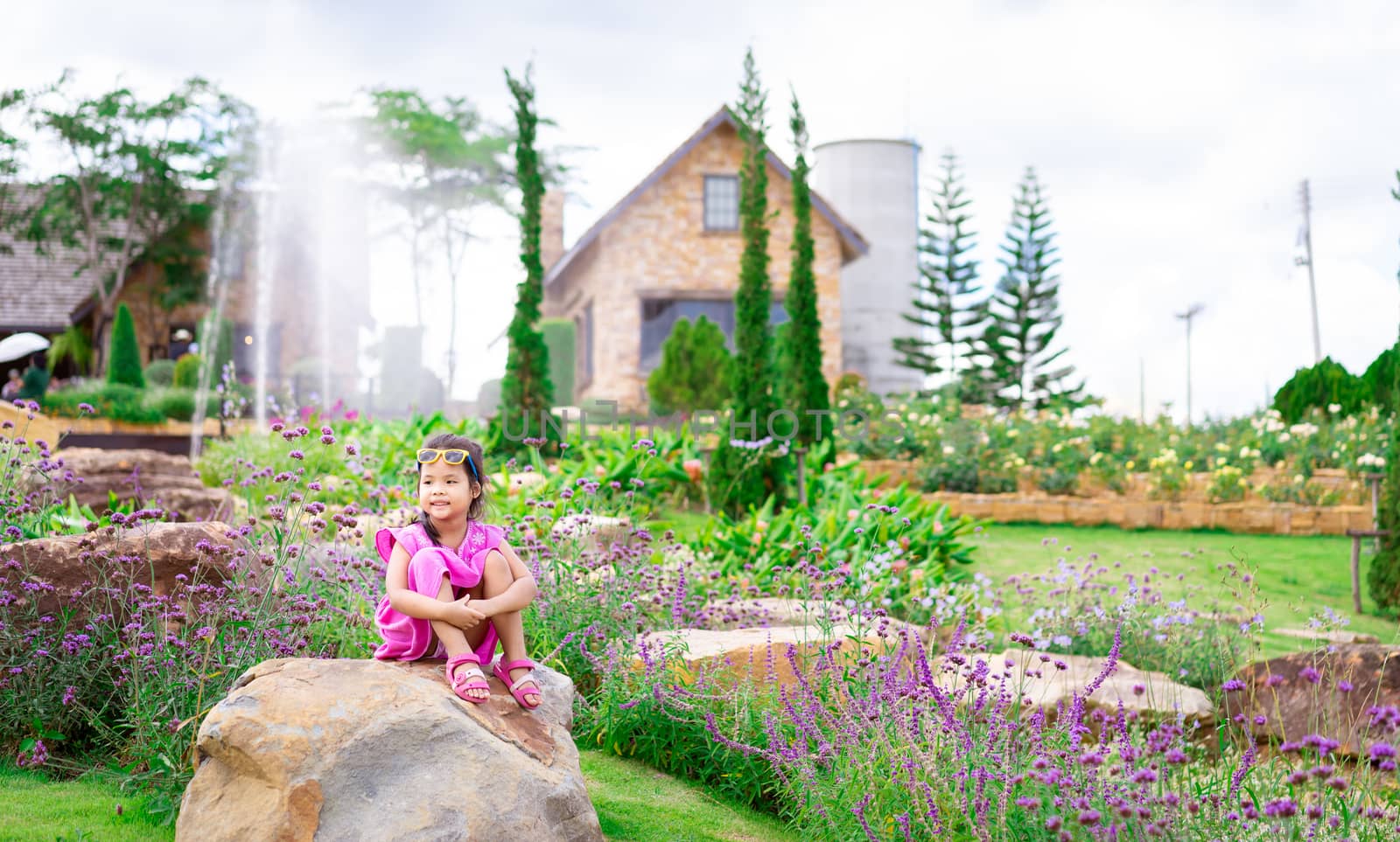 little asian girl in pink dress sitting on the rock in flower garden