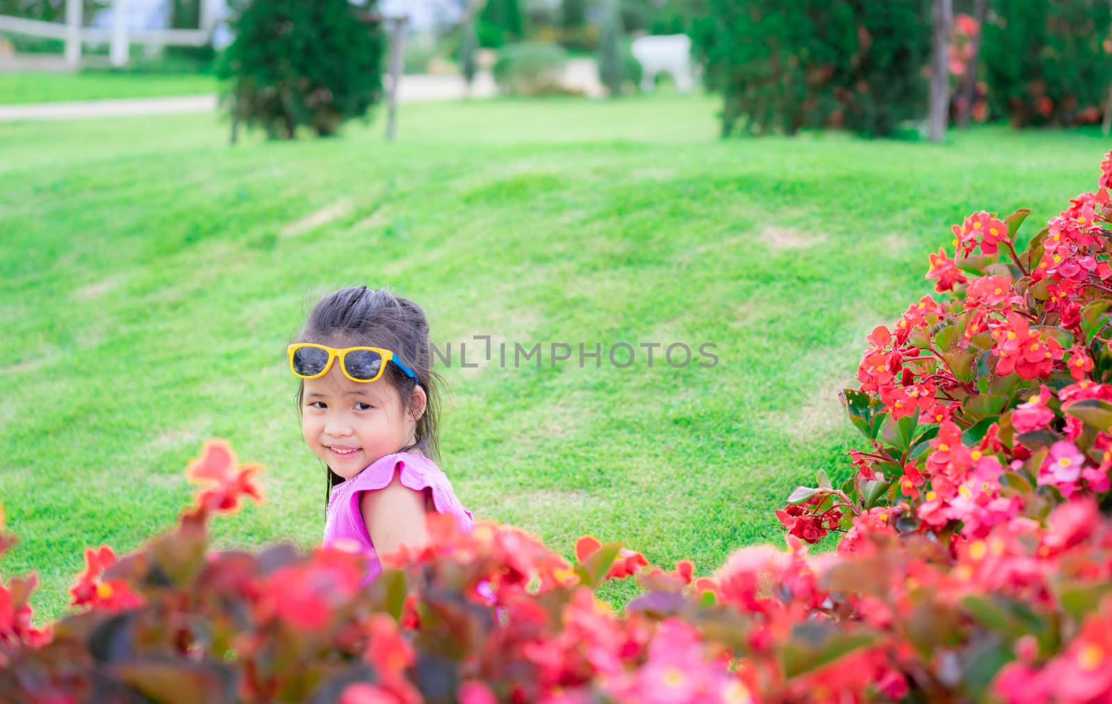 little asian girl in pink dress sitting on the ground in flower garden