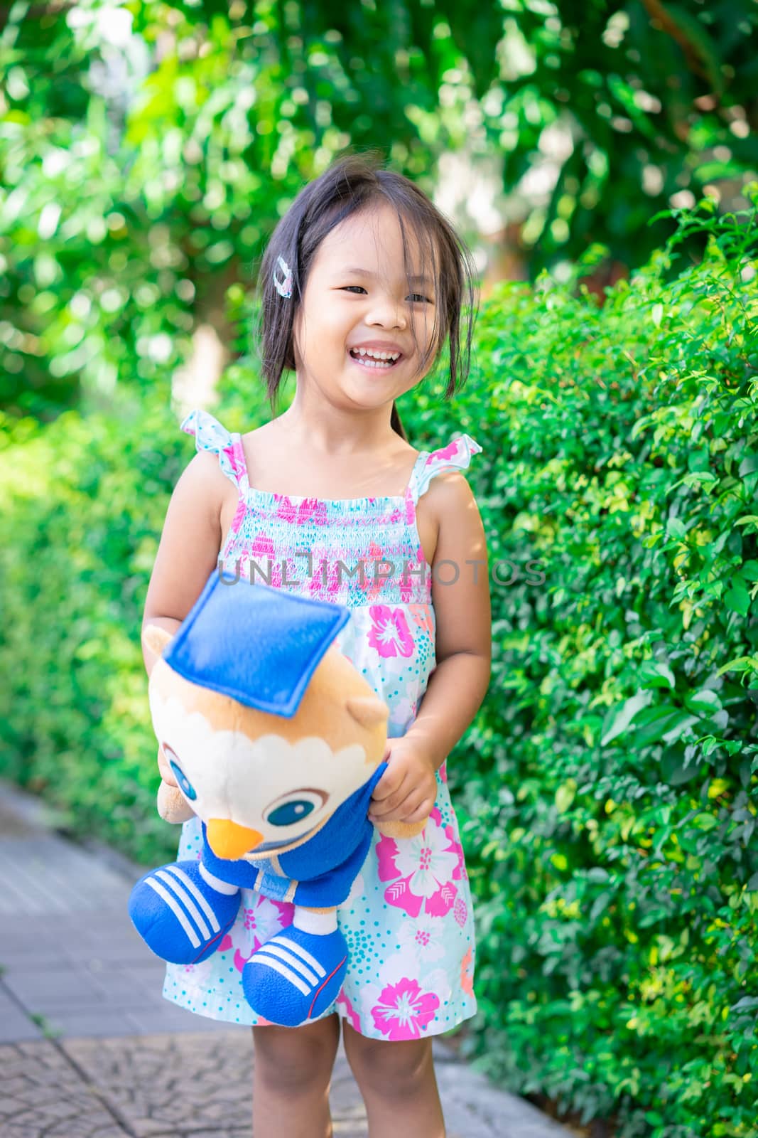 Portrait of happy asian little girl with doll standing on footpath in the park