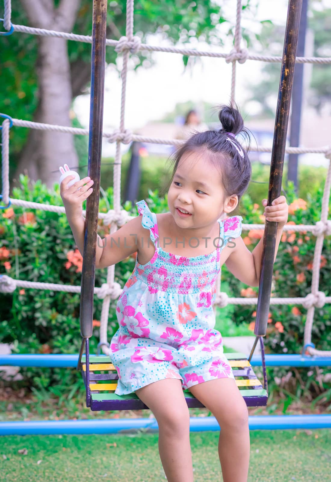 Little girl in dress sitting on a swing in the park by domonite