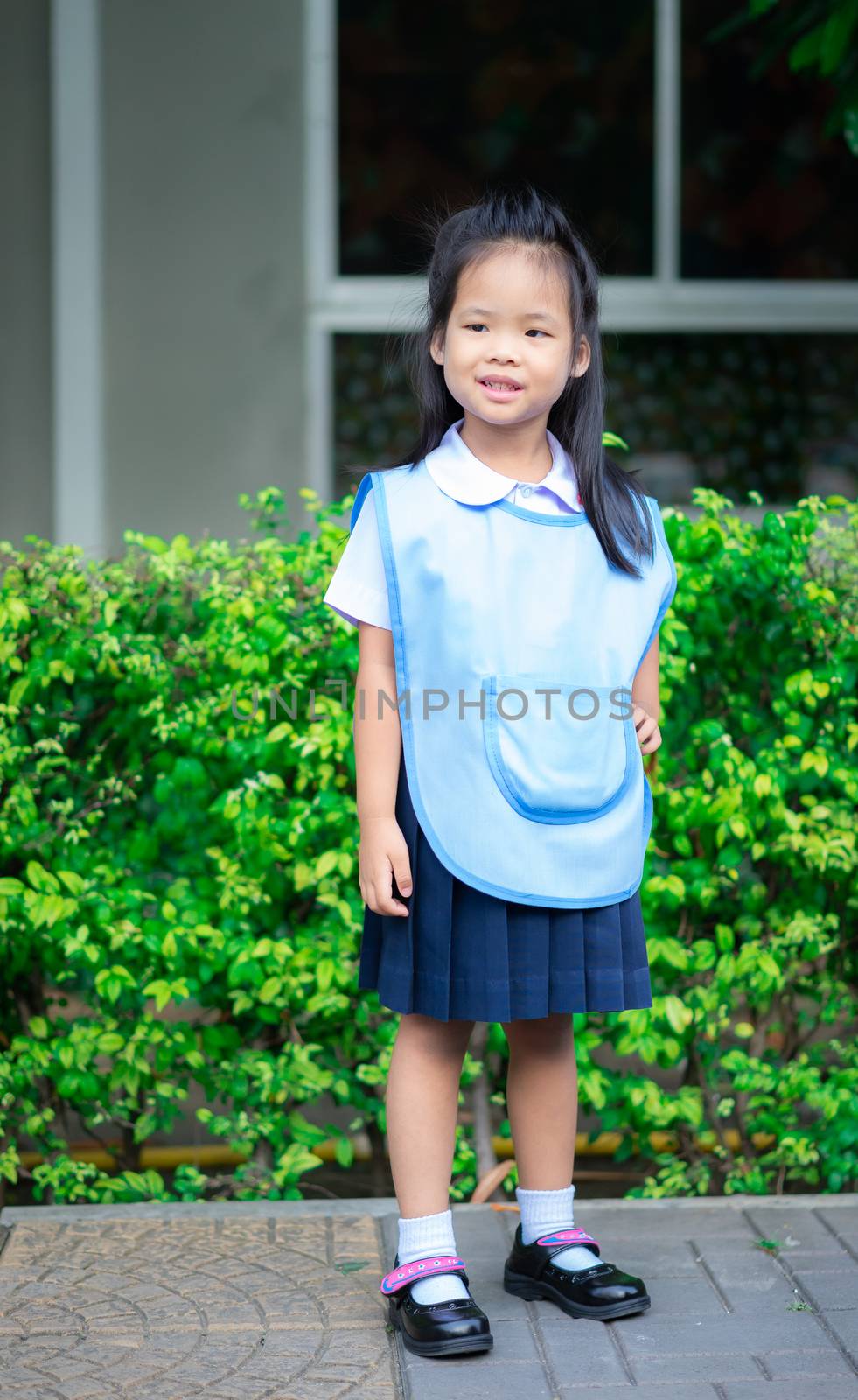 Portrait of happy little girl in Thai school uniform standing on footpath, ready back to school