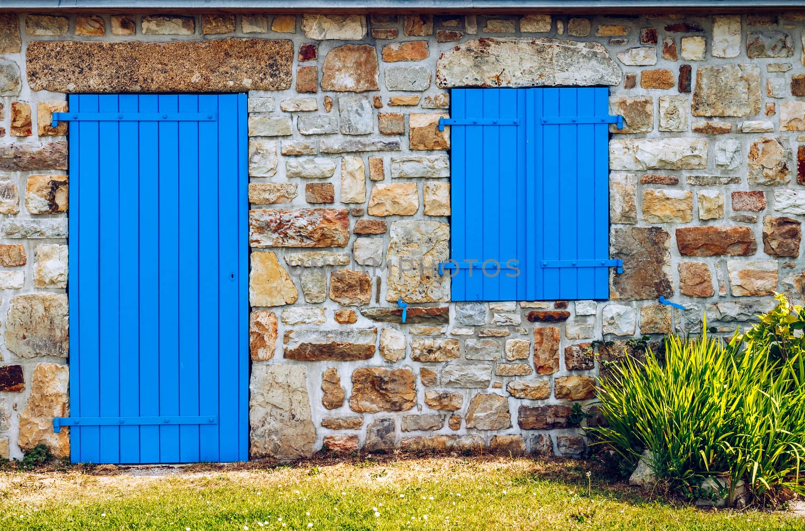 Vintage blue door and window on the facade of an old cottage stone wall.
