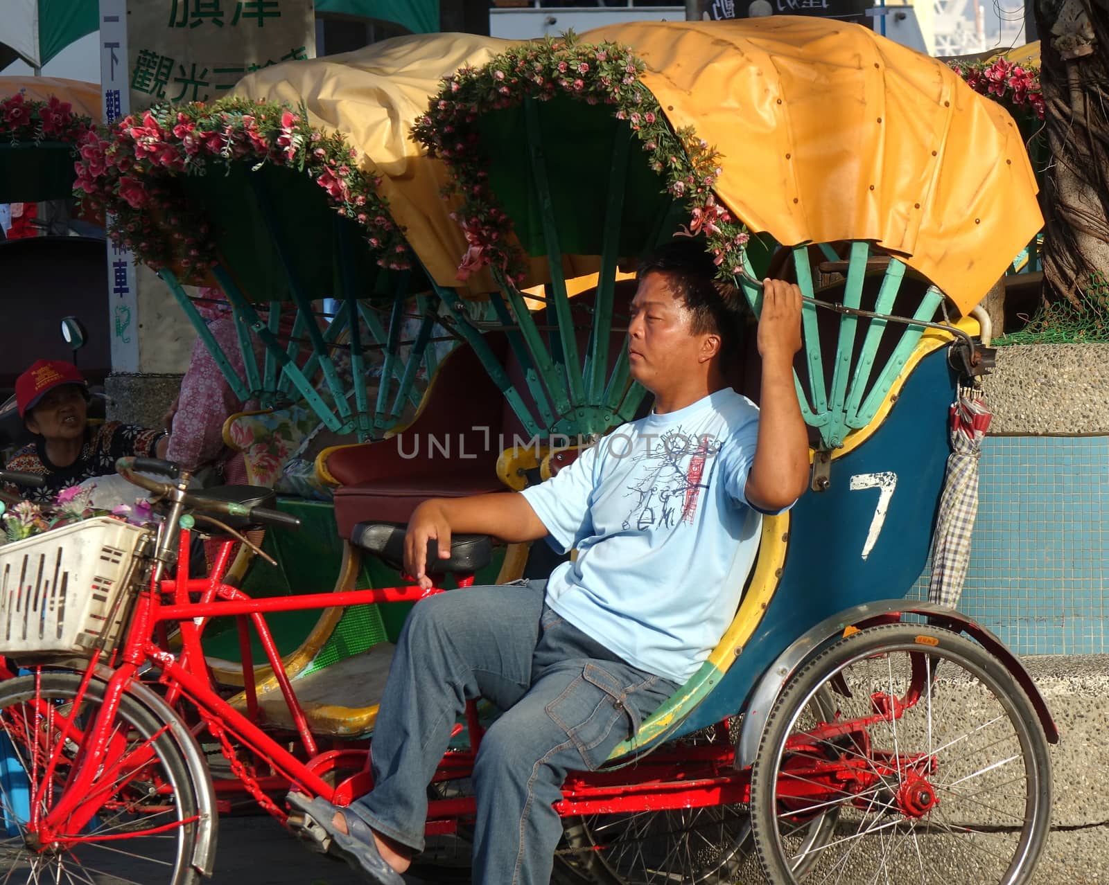 KAOHSIUNG, TAIWAN -- DECEMBER 22, 2018: A driver for a traditional cycle rickshaw rests in the afternoon sun while waiting for passengers.
