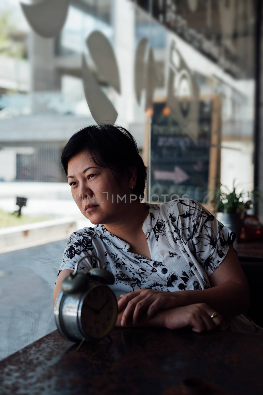 Asian woman 40s white skin plump body in black and white shirt have a bored and unhappy gesture between waiting something in a coffee shop cafe with a clock vintage style